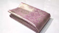 A close-up of an elegant baby pink Kanchipuram tissue silk saree with intricate gold brocade weaving, authentic Silk Mark certification, and a soft, lustrous metallic sheen.