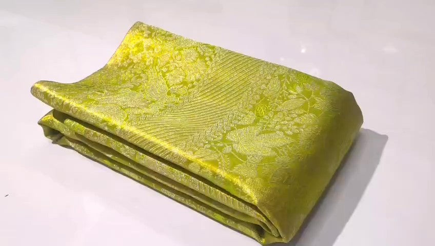 A close-up of a vibrant lime green Kanchipuram tissue silk saree with intricate gold brocade weaving and a lustrous metallic finish.