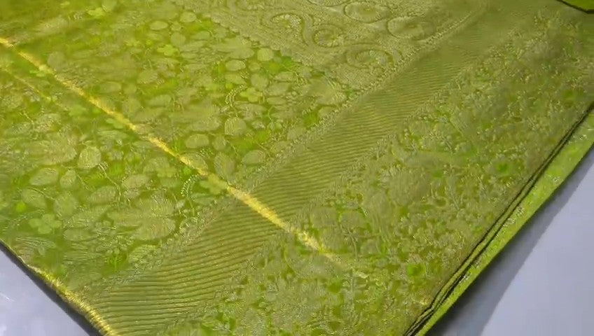 A close-up of a vibrant lime green Kanchipuram tissue silk saree with intricate gold brocade weaving and a lustrous metallic finish.