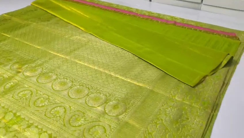 A close-up of a vibrant lime green Kanchipuram tissue silk saree with intricate gold brocade weaving and a lustrous metallic finish.