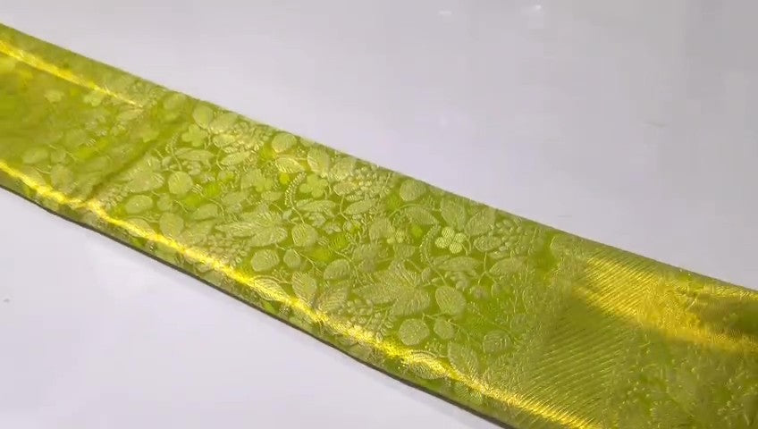 A close-up of a vibrant lime green Kanchipuram tissue silk saree with intricate gold brocade weaving and a lustrous metallic finish.