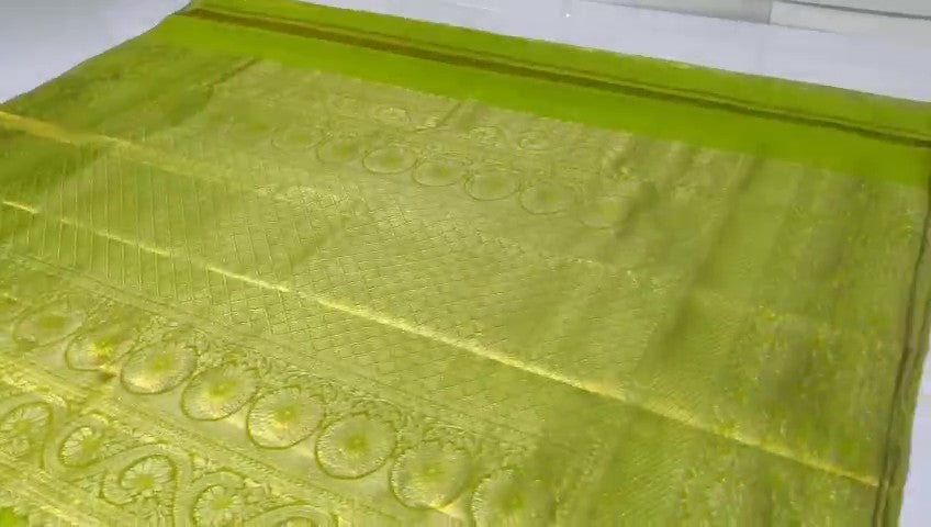 A close-up of a vibrant lime green Kanchipuram tissue silk saree with intricate gold brocade weaving and a lustrous metallic finish.