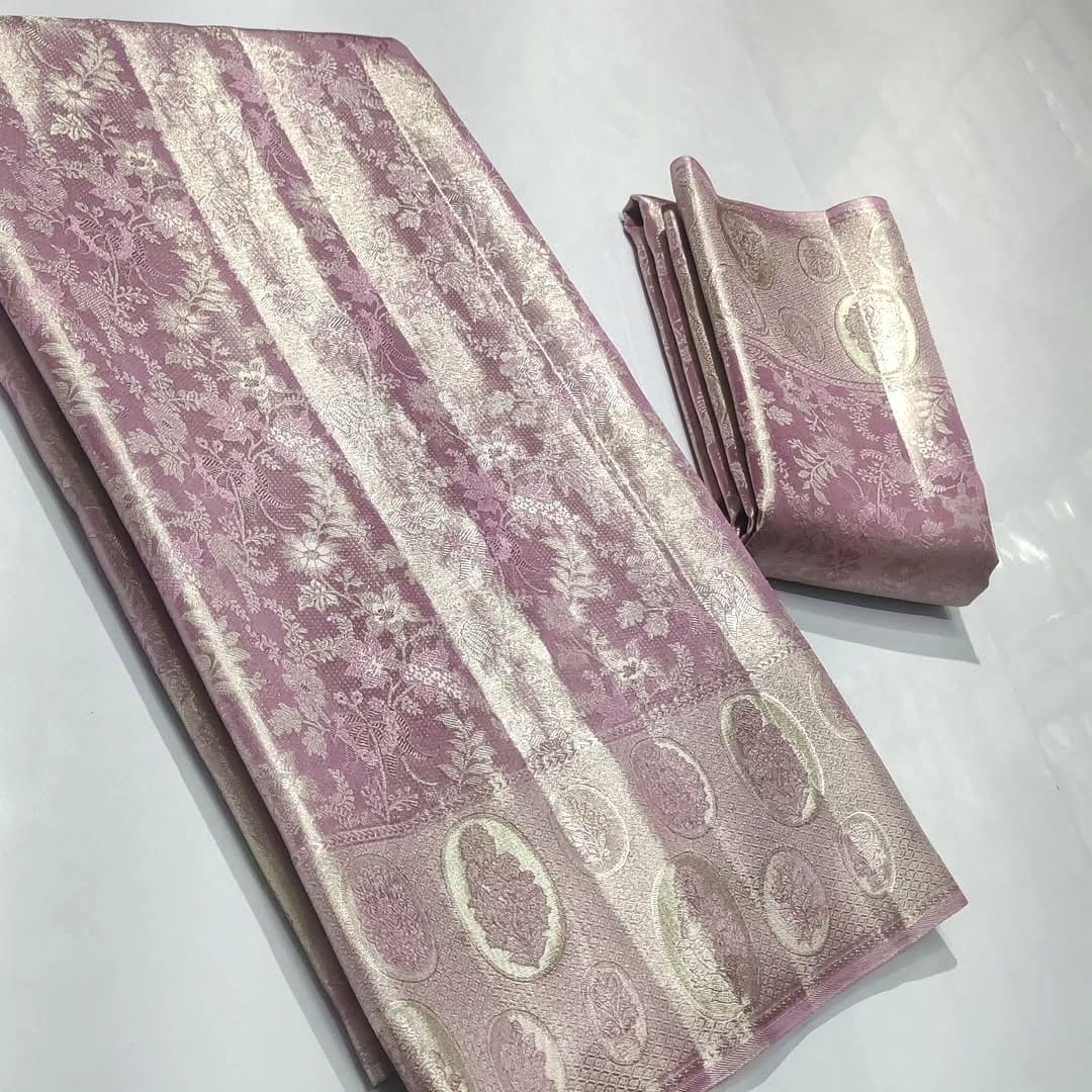 A close-up of an elegant baby pink Kanchipuram tissue silk saree with intricate gold brocade weaving, authentic Silk Mark certification, and a soft, lustrous metallic sheen.