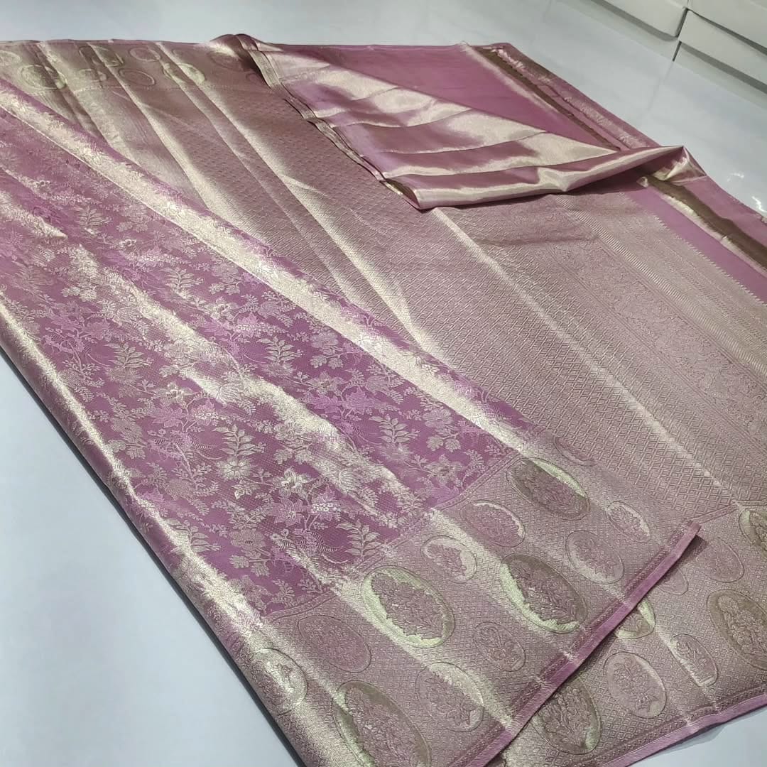 A close-up of an elegant baby pink Kanchipuram tissue silk saree with intricate gold brocade weaving, authentic Silk Mark certification, and a soft, lustrous metallic sheen.