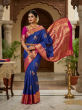 A model elegantly draped in a royal blue Kanchipuram semi pattu silk saree featuring intricate gold zari stripes, multicolored chakram motifs, and a contrasting magenta-pink border with detailed gold floral patterns.