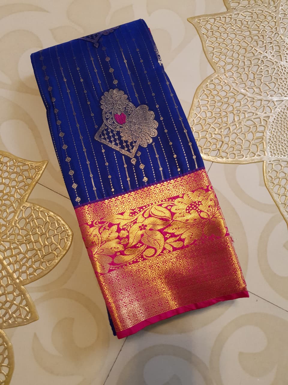 Royal blue Kanchipuram semi pattu silk saree featuring intricate gold zari stripes, multicolored chakram motifs, and a contrasting magenta-pink border with detailed gold floral patterns.