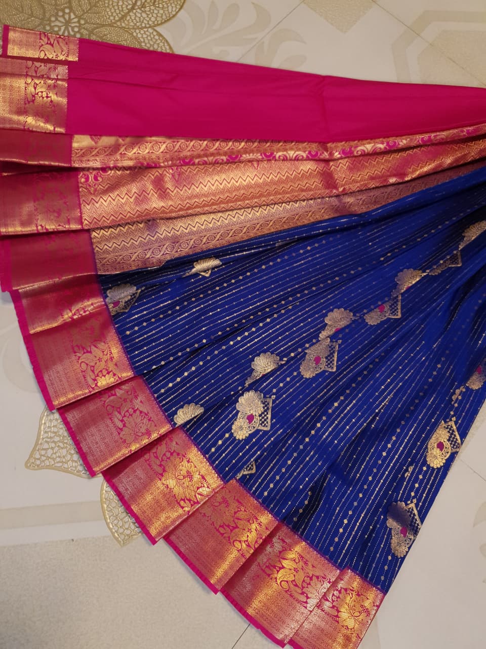 Royal blue Kanchipuram semi pattu silk saree featuring intricate gold zari stripes, multicolored chakram motifs, and a contrasting magenta-pink border with detailed gold floral patterns.