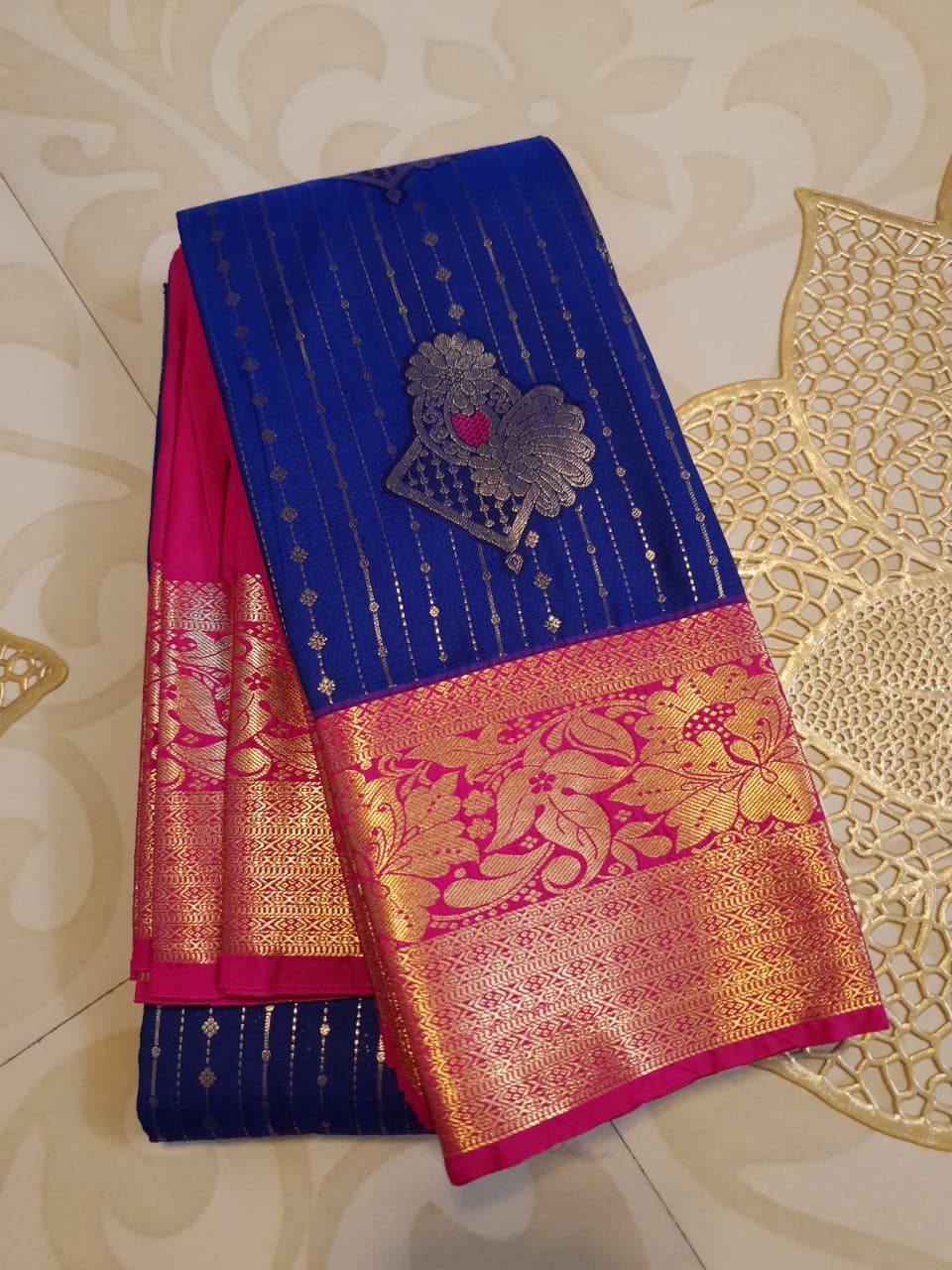Royal blue Kanchipuram semi pattu silk saree featuring intricate gold zari stripes, multicolored chakram motifs, and a contrasting magenta-pink border with detailed gold floral patterns.