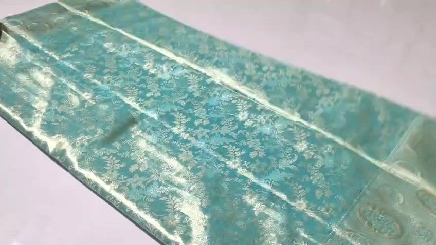 A close-up of a light aqua blue fabric with a subtle floral brocade pattern, laid flat on a light background.
