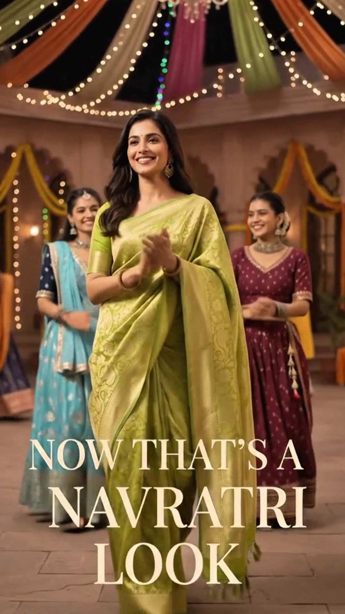 A woman in a light green saree stands in a decorated indoor setting with other women in colorful traditional outfits in the background. Large text at the bottom reads, 'NOW THAT'S A NAVRATRI LOOK.