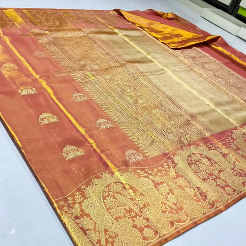 A close-up of a luxurious burnt orange Kanchipuram tissue silk saree with intricate gold brocade weaving, authentic Silk Mark certification, and a shimmering metallic finish.