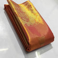 A close-up of a luxurious burnt orange Kanchipuram tissue silk saree with intricate gold brocade weaving, authentic Silk Mark certification, and a shimmering metallic finish.