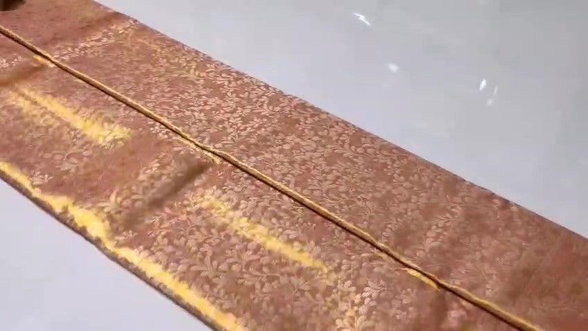 A close-up view of a Dusty Rose Kanchipuram tissue silk saree featuring elegant gold floral brocade patterns and authentic handloom texture.