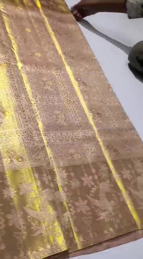 A close-up of a luxurious gold Kanchipuram tissue silk saree featuring intricate metallic brocade weaving, authentic Silk Mark certification, and a grand bridal luster.