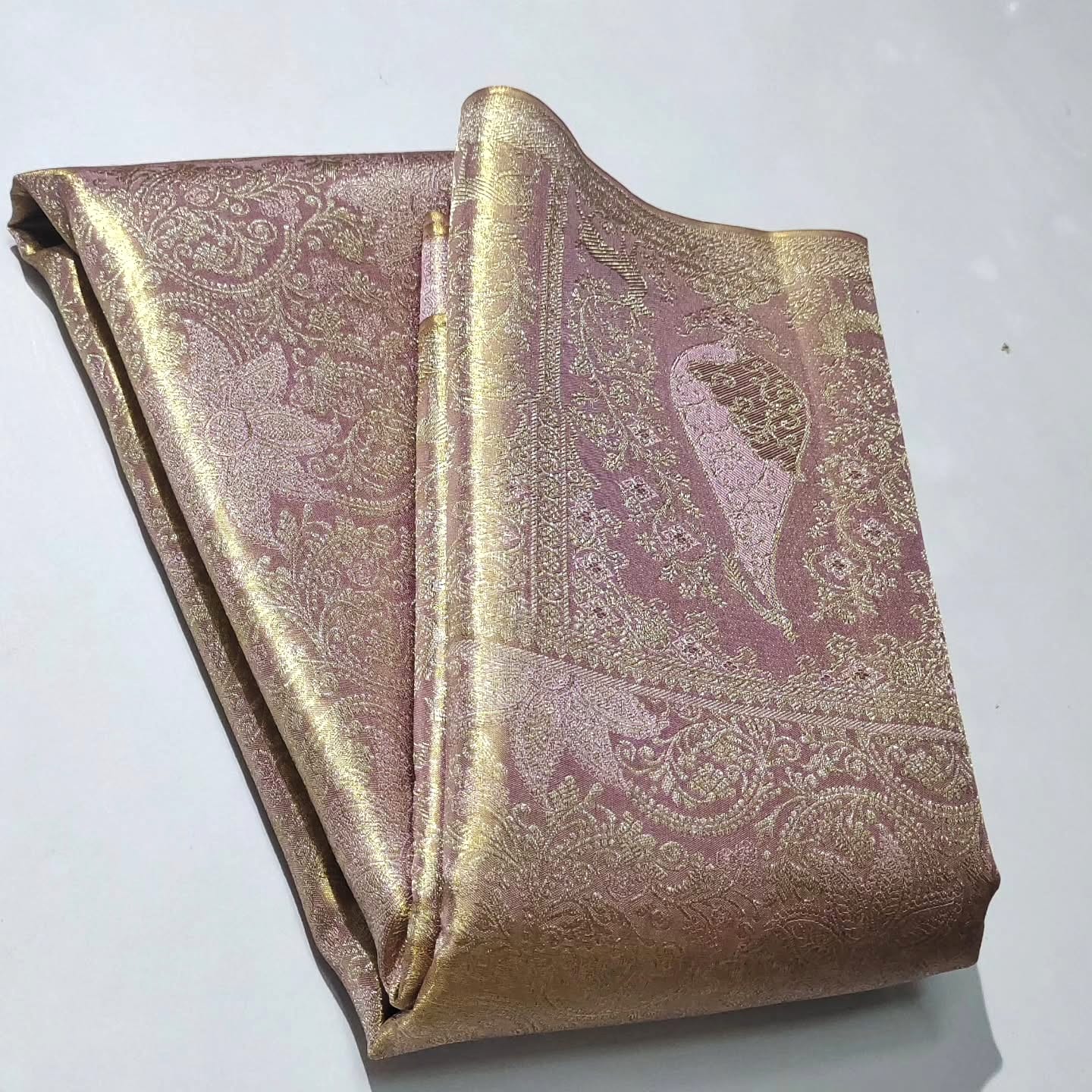 Neatly folded baby pink Kanchipuram handloom tissue silk saree displaying the rich pallu and shimmering metallic finish.
